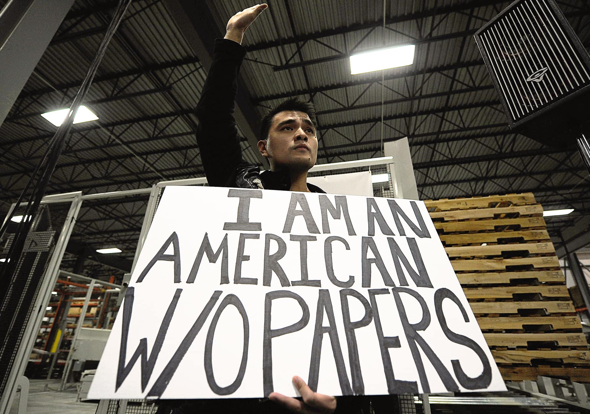 Jose Antonio Vargas holding a protest sign saying 'I am an American w/o papers' and raising his hand.