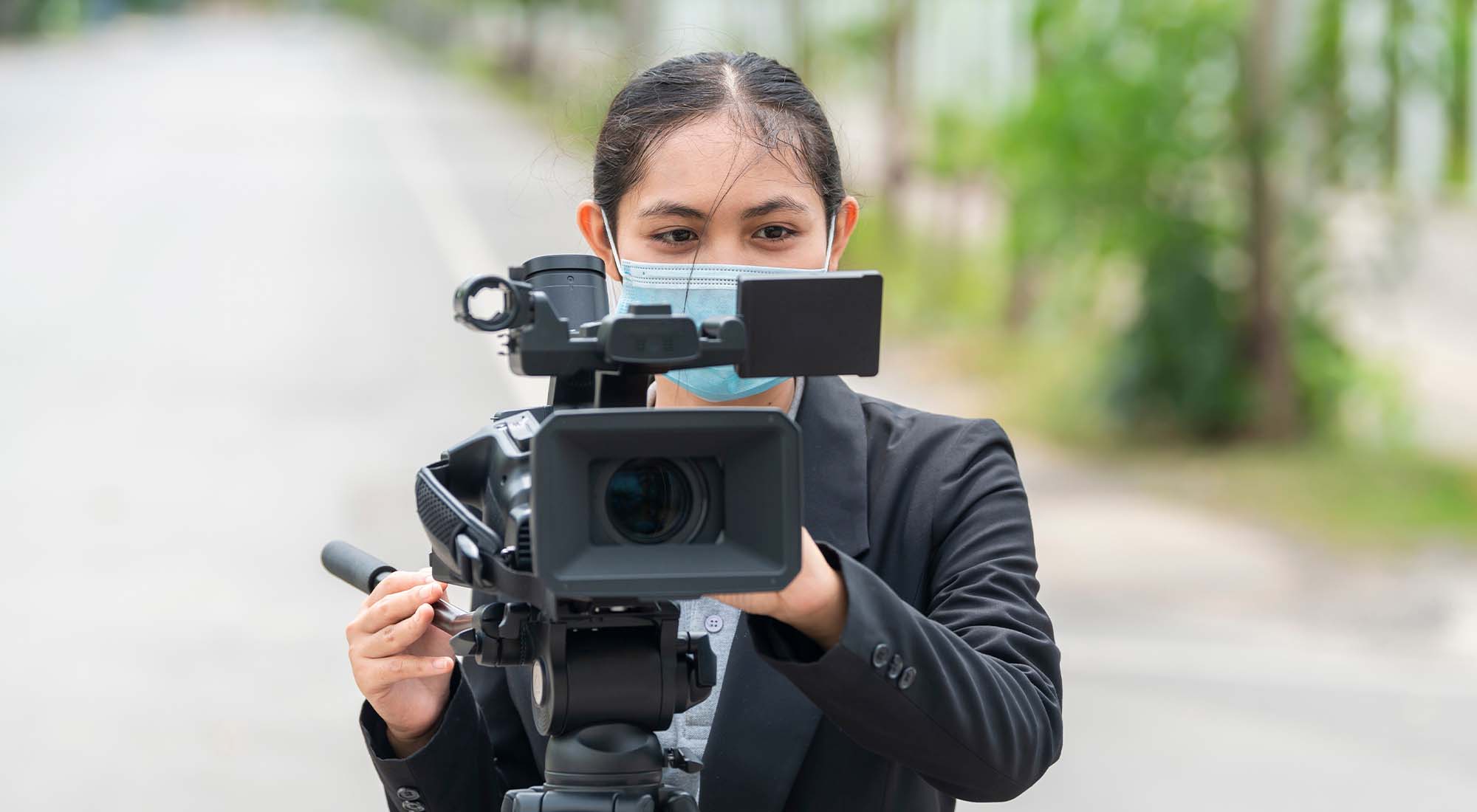 An Asian woman in business casual filming with a professional camera.